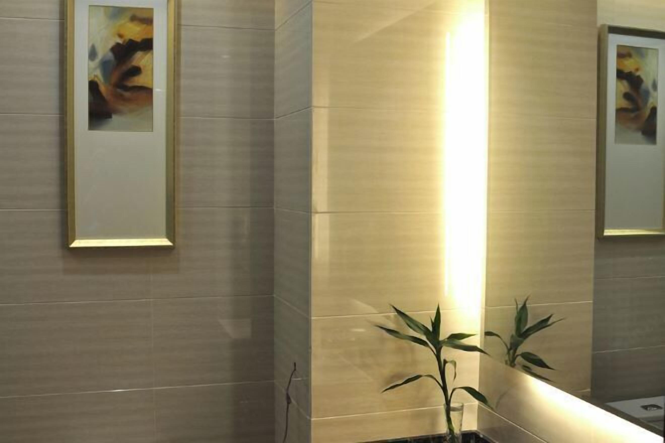 A modern bathroom with a large mirror, framed artwork, and a potted plant.