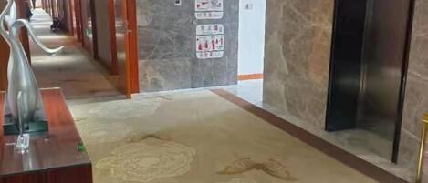 A hotel corridor with a marble wall, a reception desk, and an elevator.
