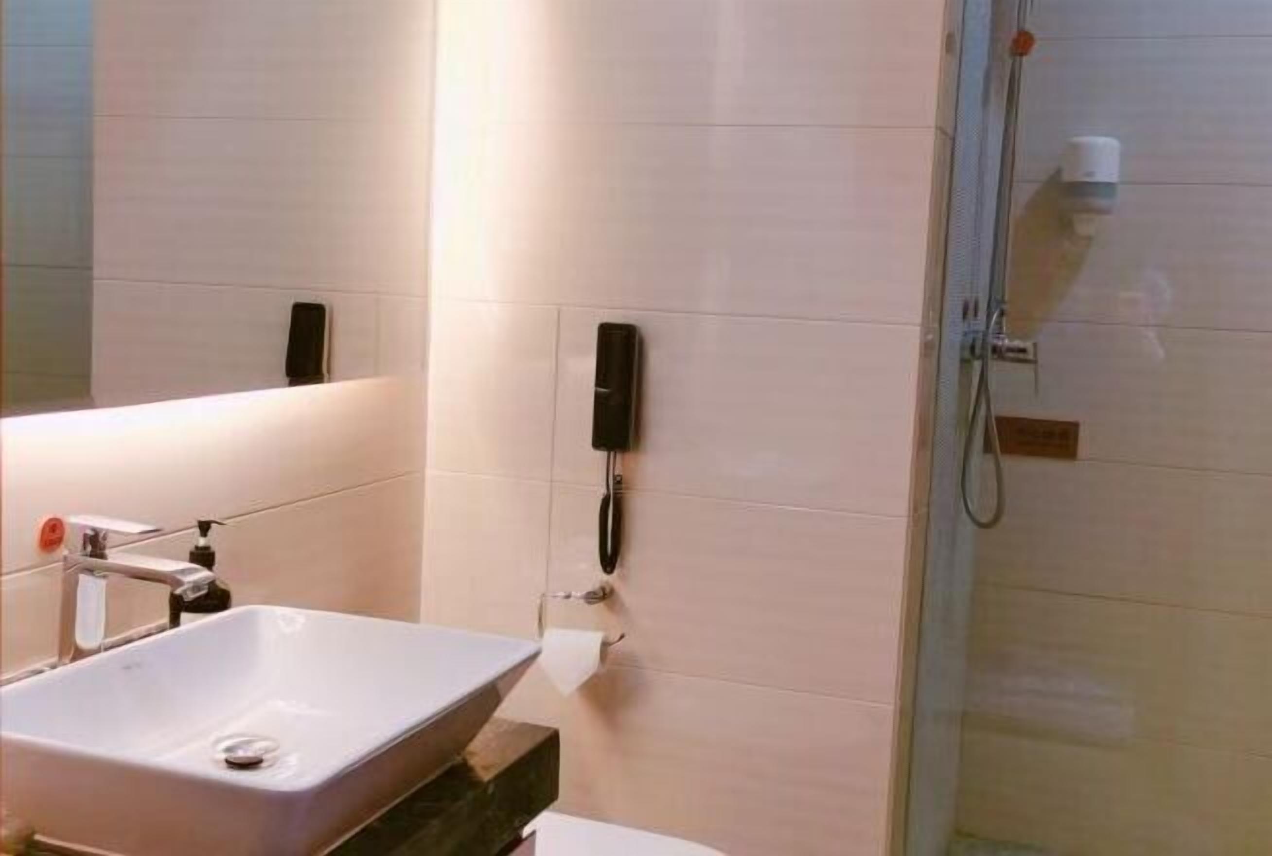 A bathroom with a sink, a mirror, a toilet, a shower, and a telephone mounted on the wall.