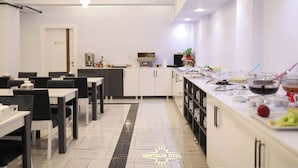 A modern dining area with white and black furniture, a kitchen counter with food items, and a chandelier. - Vantalya Otel (Van)