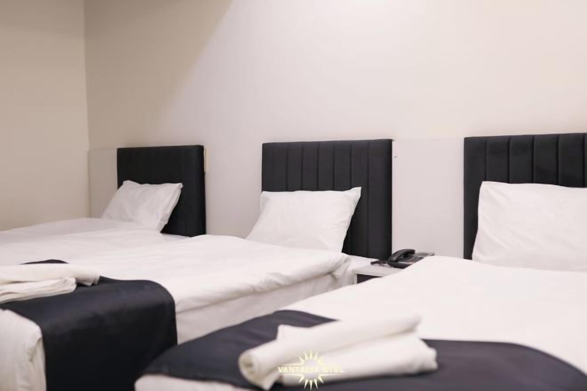 A hotel room with three beds, each with a black headboard and white bedding.
