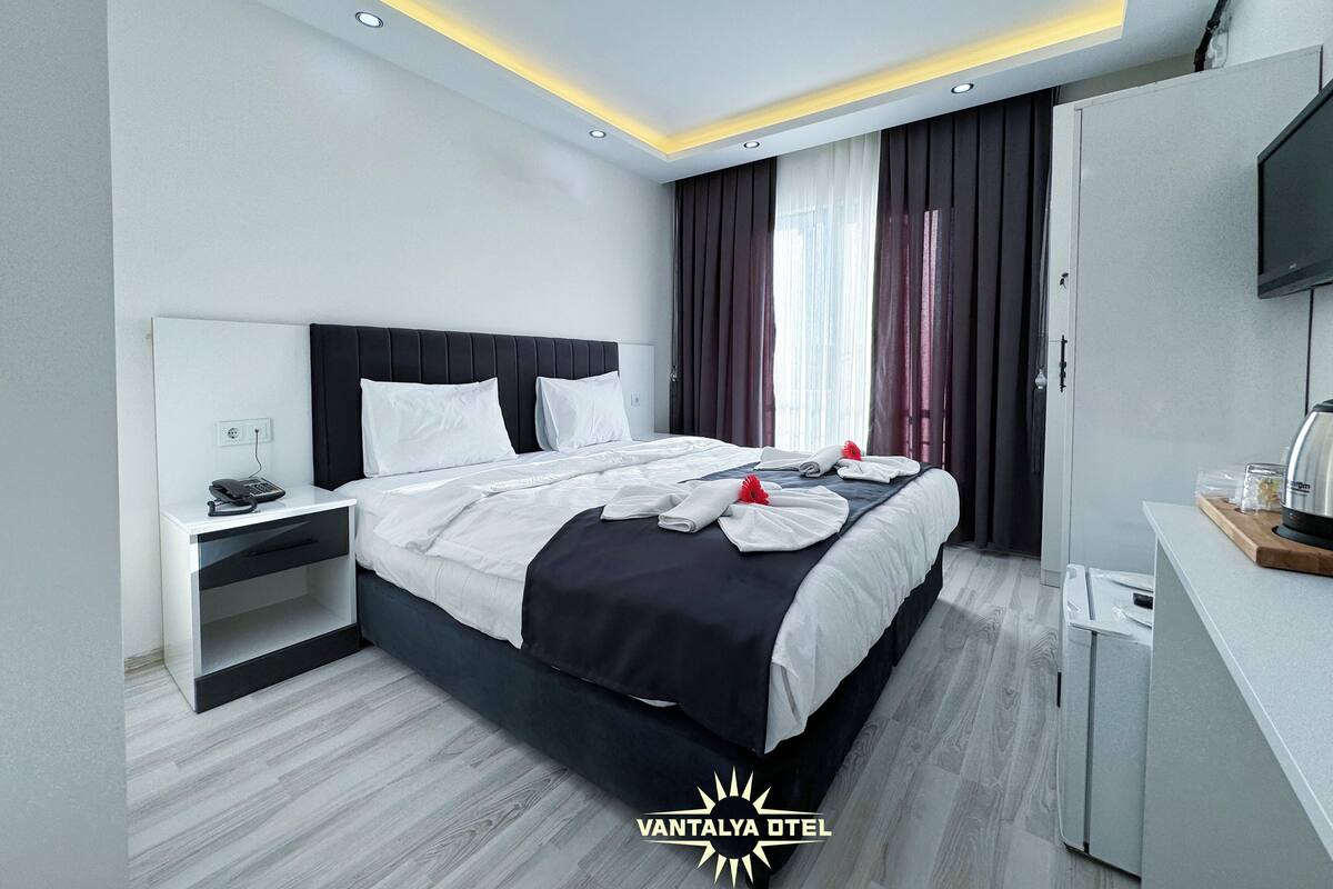 A modern hotel room with a large bed, bedside tables, a flat-screen TV, and a built-in washing machine.