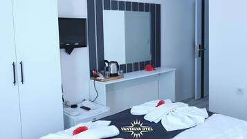 Habitación de hotel con cama, armario, espejo, una mesita con hervidor y un adorno rojo.