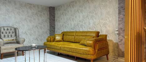 A living room with a yellow leather sofa, a grey armchair, and a glass-top coffee table.