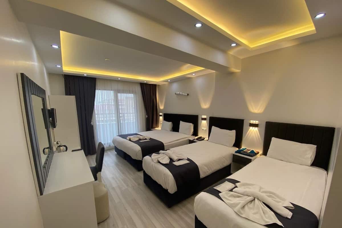 A hotel room with three beds, a desk, and a mirror.