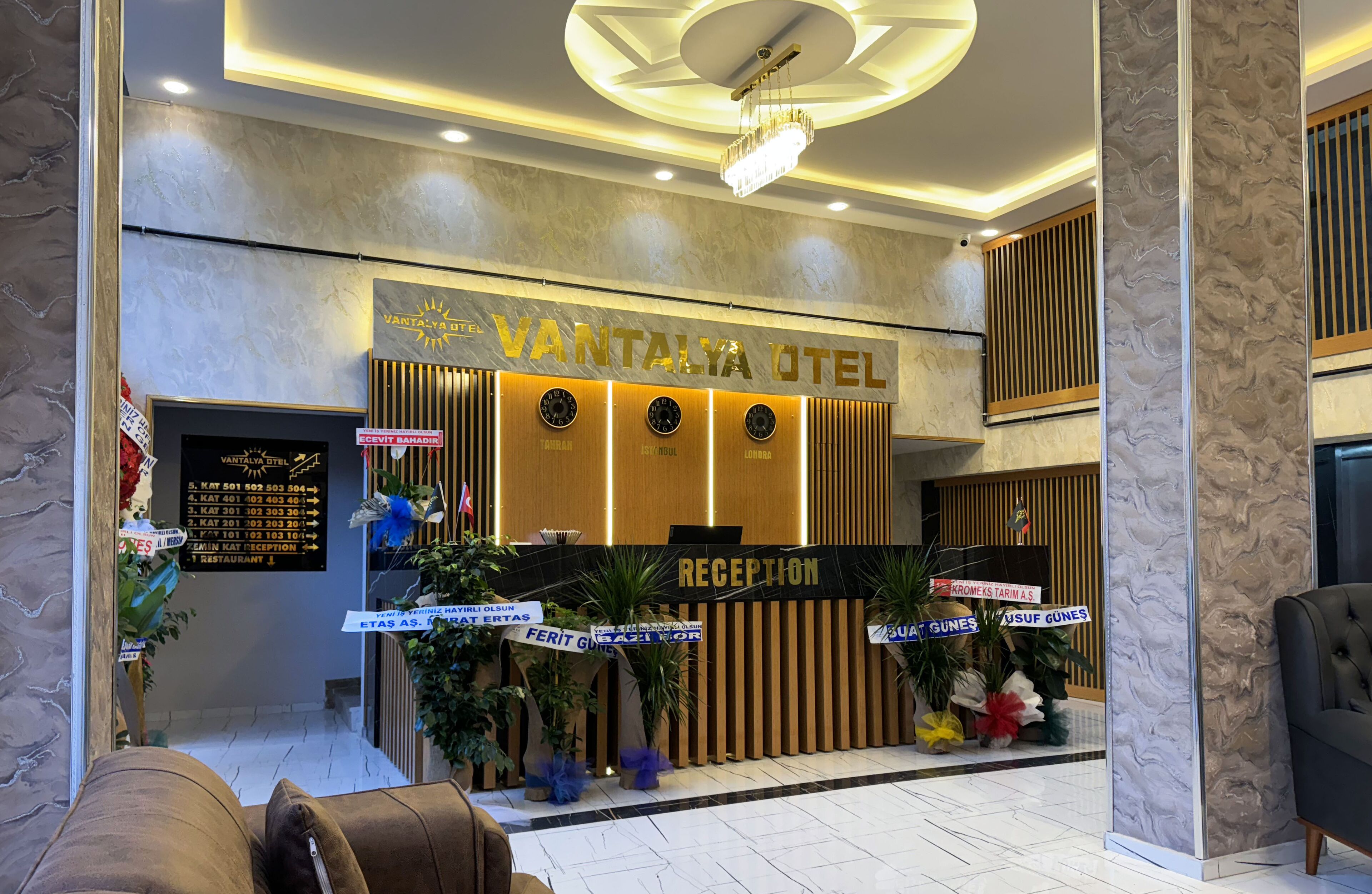 A hotel reception area with a modern design, including a reception desk, a chandelier, and a sign for 'VANTALYA HOTEL'.