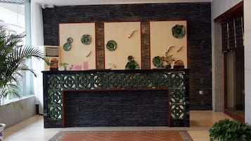 A reception area with a dark wood reception desk, decorative wall panels, and potted plants.