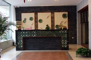 A reception area with a dark wood reception desk, decorative wall panels, and potted plants. - Danxia Shanyang Yuancun Inn (core scenic spot) (Renhua)