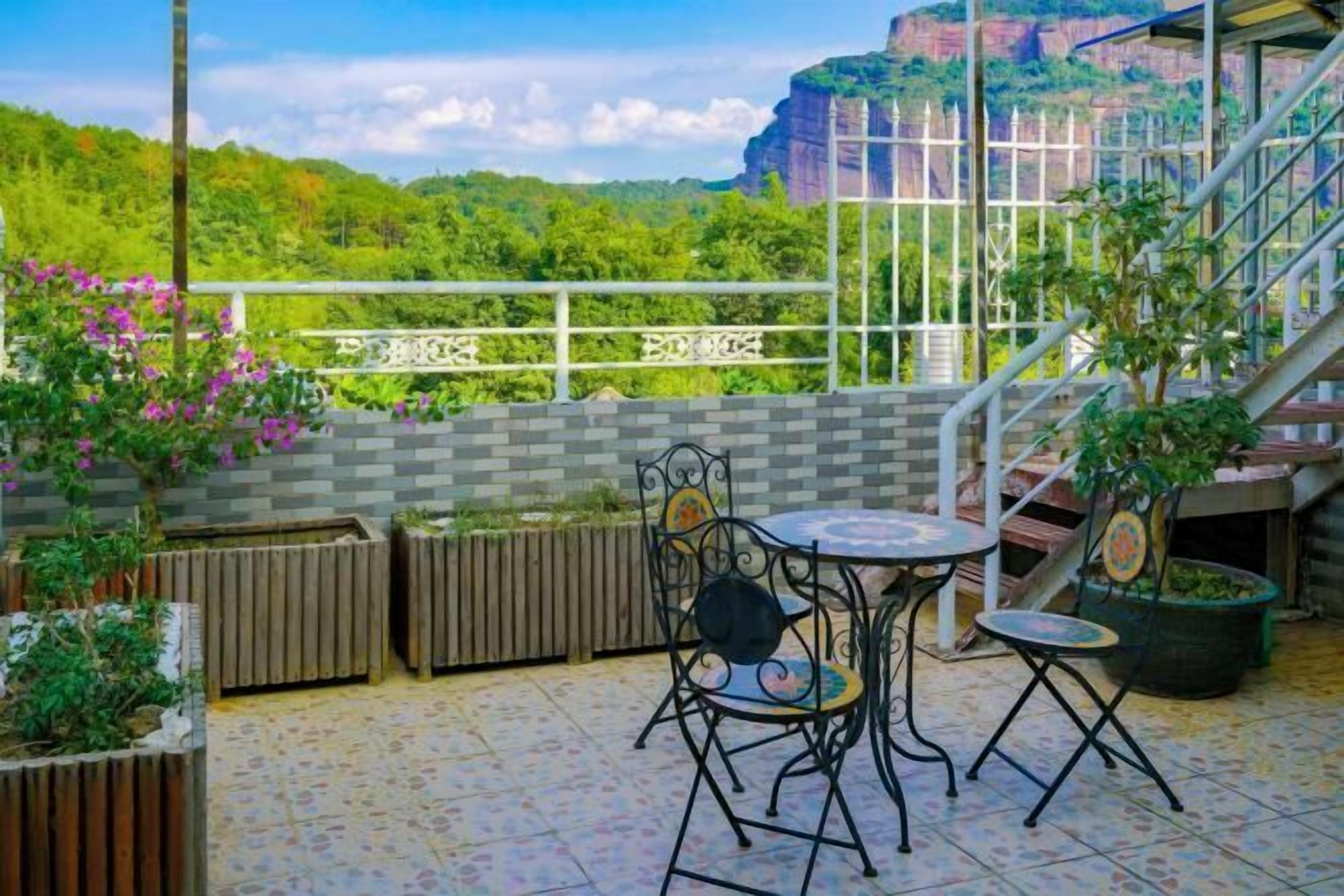 A terrace with a table and chairs, a view of greenery and a building in the background.