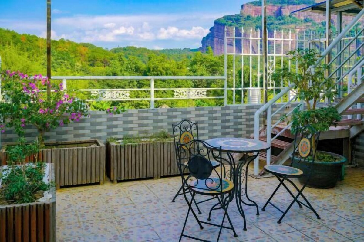 A terrace with a table and chairs, a view of greenery and a building in the background.