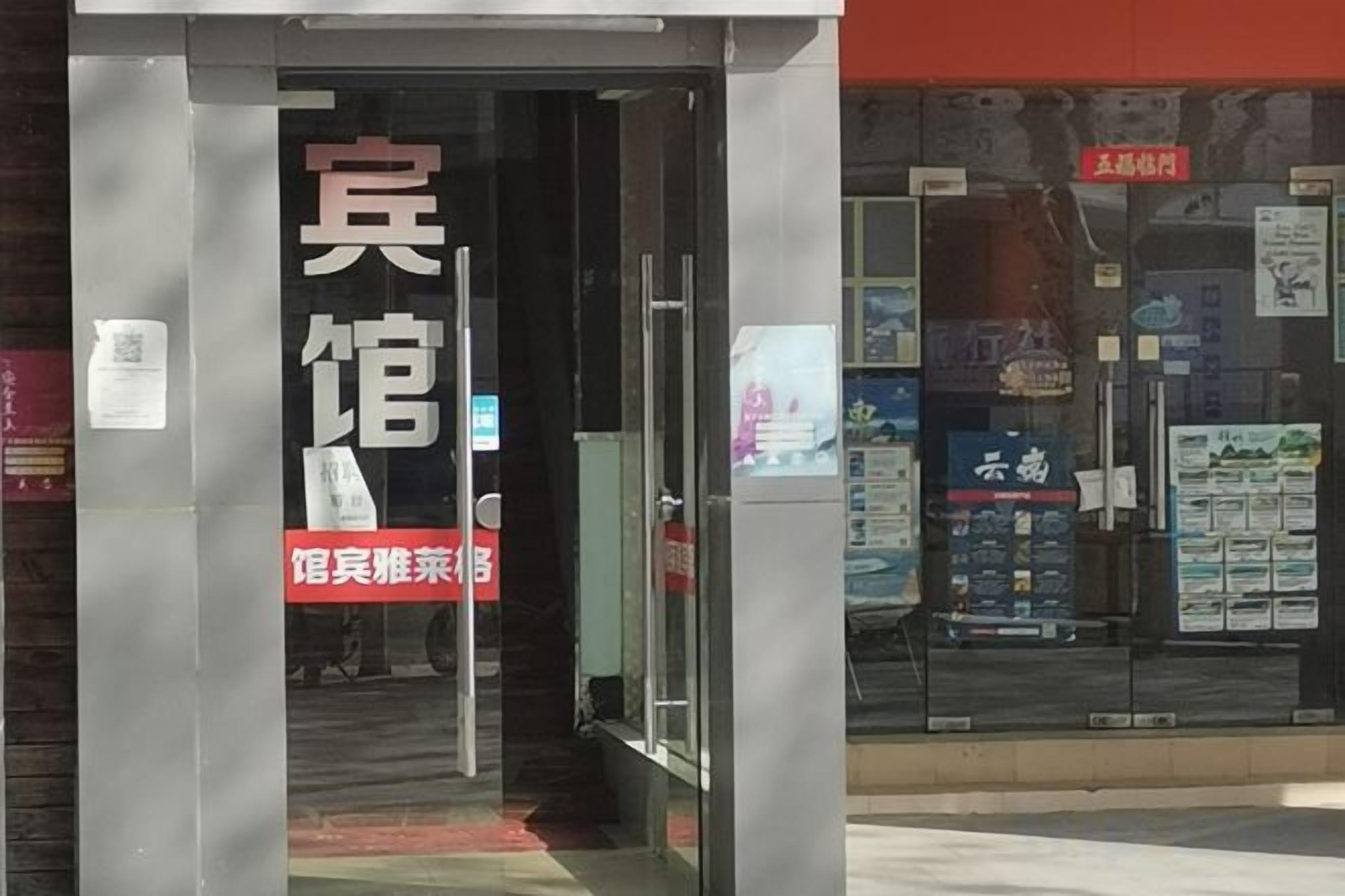 A hotel entrance with a glass door, a signboard, and a red banner.