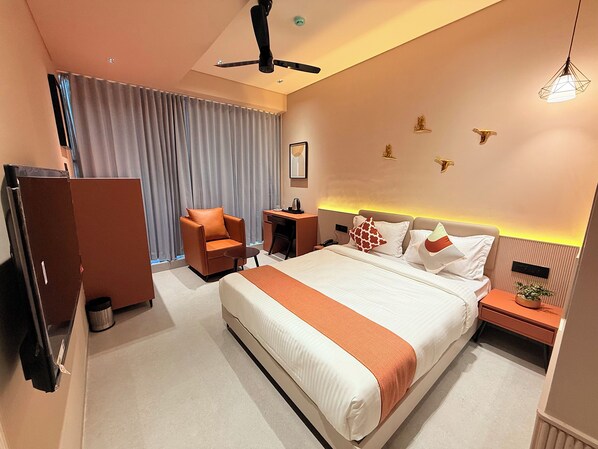 A modern hotel room with a large bed, a desk, a chair, and a ceiling fan. - Hotel Fun Regency (Ahmedabad)