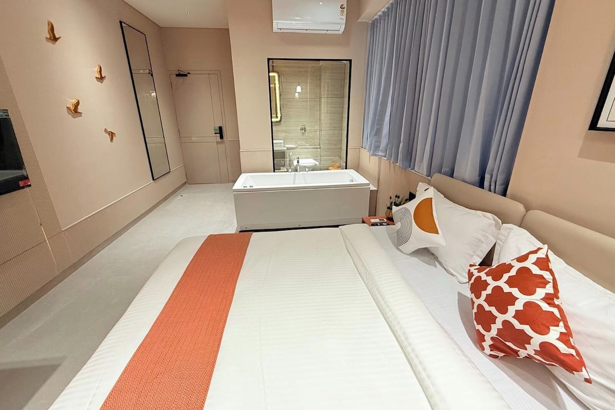 A modern hotel room with a large bed, a separate bathroom, and a large window with curtains.