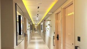 A modern hotel corridor with a long, straight layout, recessed ceiling lighting, and a reflective floor. - Hotel Fun Regency (Ahmedabad)