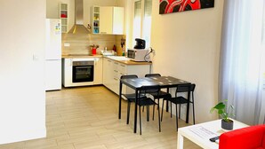 Une cuisine moderne avec des meubles blancs, un four à micro-ondes et une cuisinière. On y trouve un coin repas avec une table et des chaises, ainsi qu’un canapé rouge.