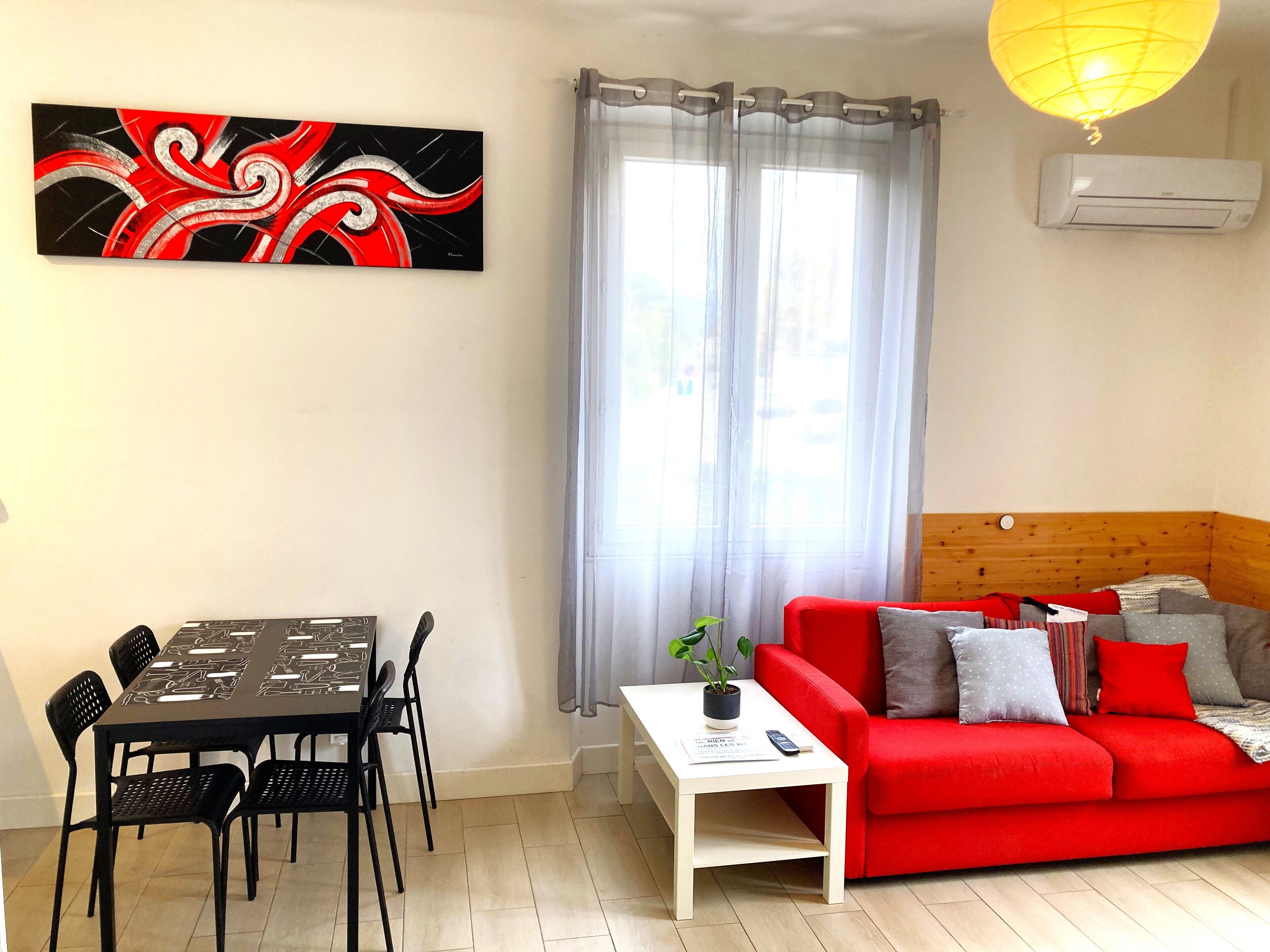 Un salon moderne avec un canapé rouge, une table à manger avec des chaises, une table basse blanche et un grand tableau abstrait accroché au mur.