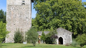 A stone tower with a small attached building, surrounded by trees and grass.