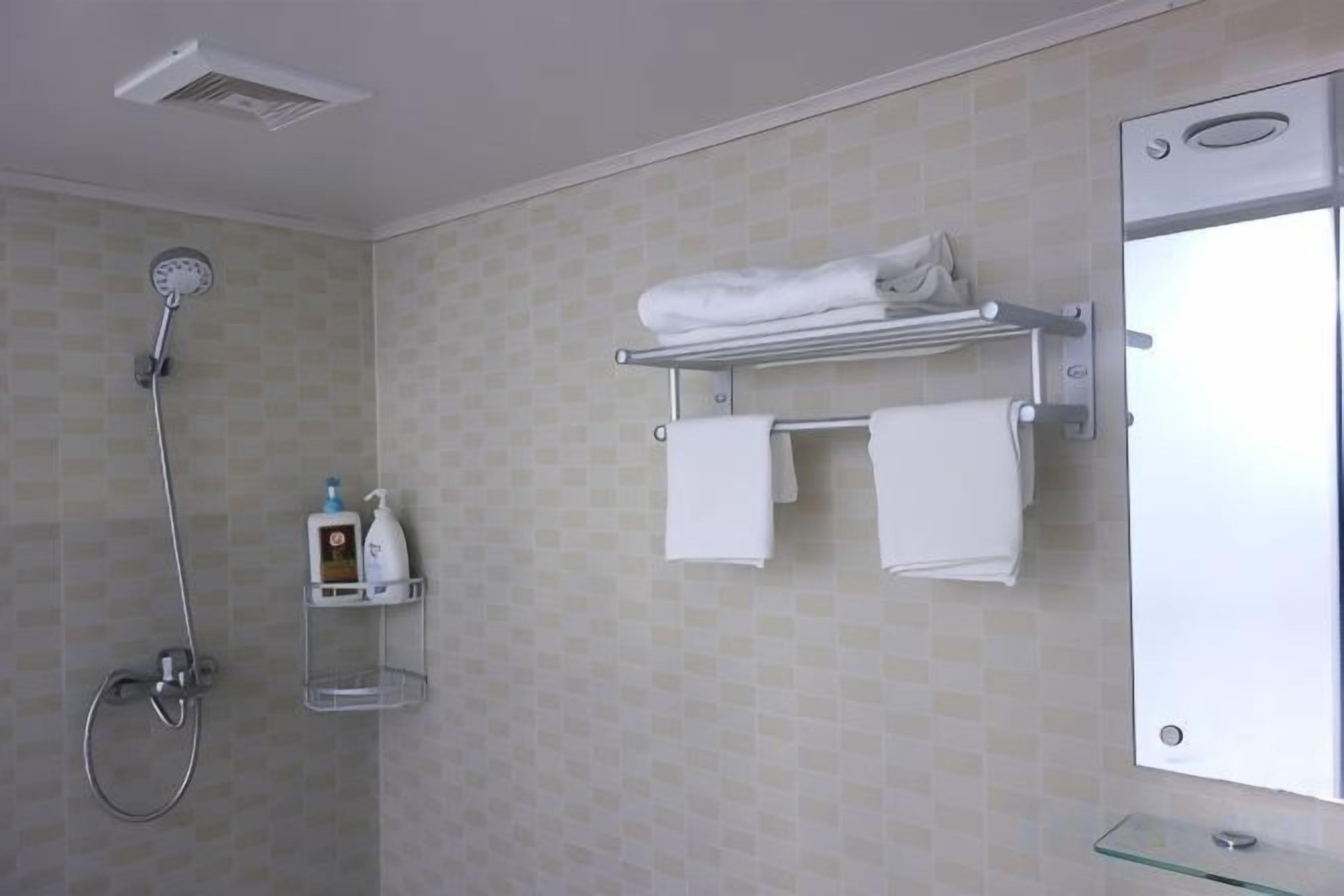 A bathroom with a shower, a towel rack with towels, and a glass shelf with toiletries.