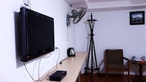 A room with a mounted TV, a tripod, a chair, and a table with a kettle. - Huike Hostel (Shanghai)