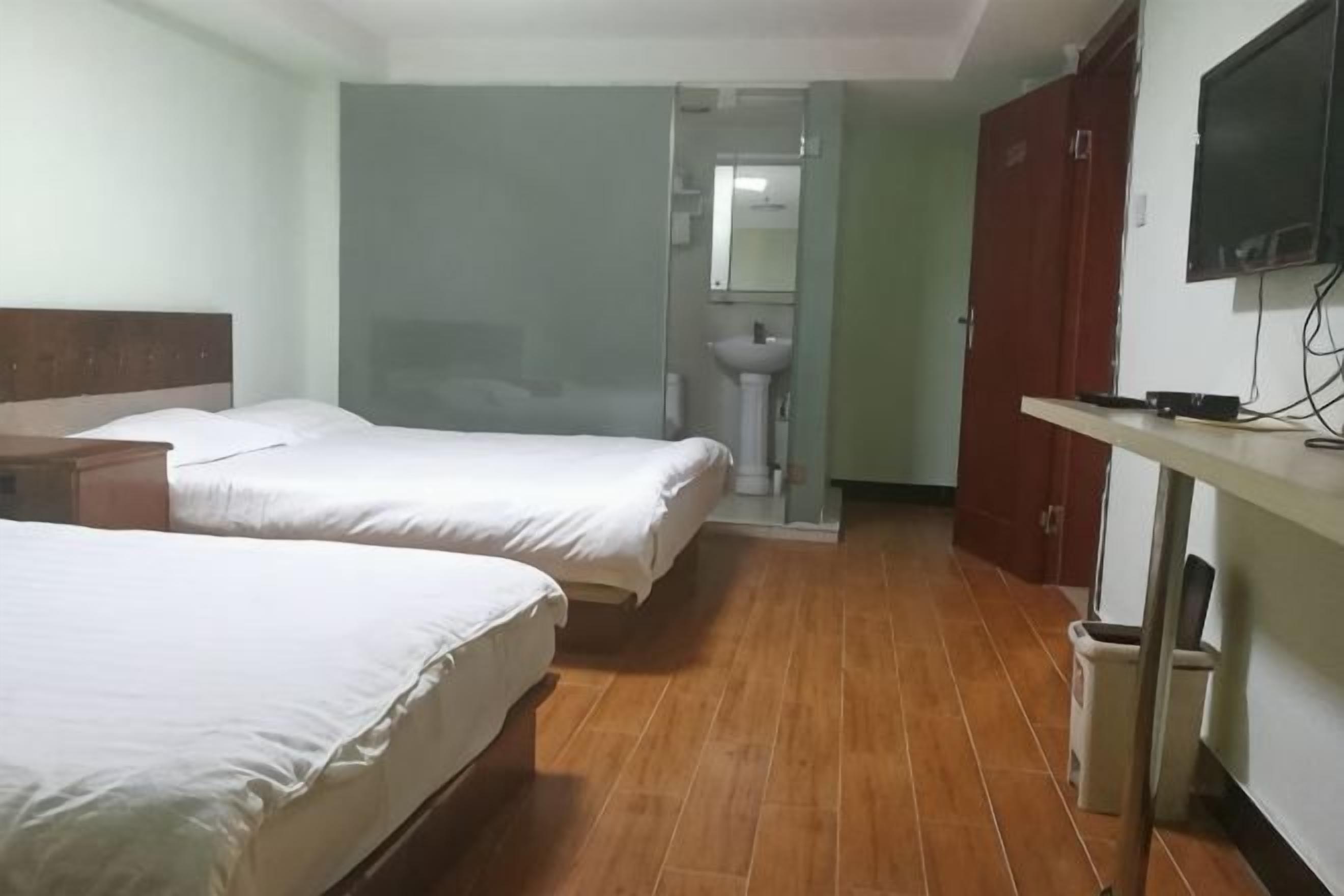 Habitación de hotel con dos camas, piso de madera, televisor, lavamanos y espejo.