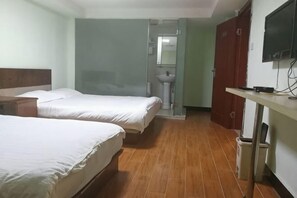 Habitación de hotel con dos camas, piso de madera, televisor, lavamanos y espejo.