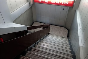 Una escalera con barandilla, paredes de baldosas y un letrero rojo con texto blanco.