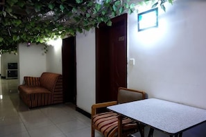 Una habitación con sofá, una mesa, sillas, una puerta y una lámpara fijada a la pared.