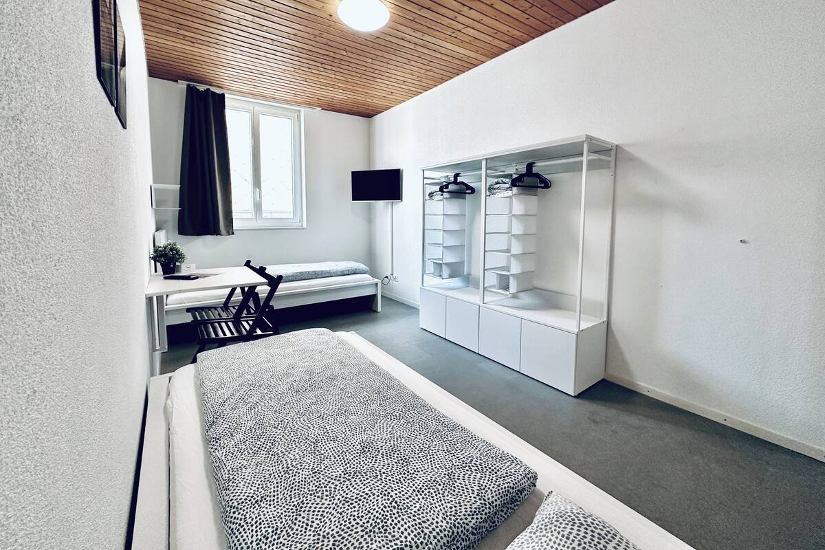 Un dormitorio moderno con una cama litera, un escritorio, un armario y un televisor fijado a la pared.