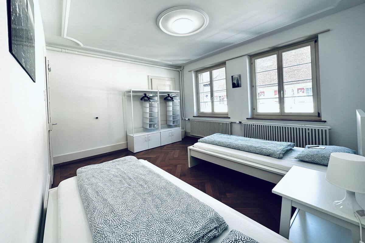 Una habitación con dos camas, un radiador, una ventana y un perchero.