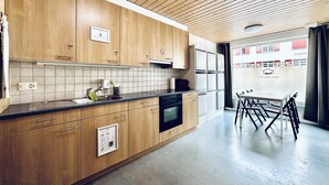 A modern kitchen with wooden cabinets, a black countertop, and a built-in oven. There is a dining area with a table and chairs visible through a glass partition. - ZIMMERzuVERMIETEN.ch Balsthal (Balsthal)