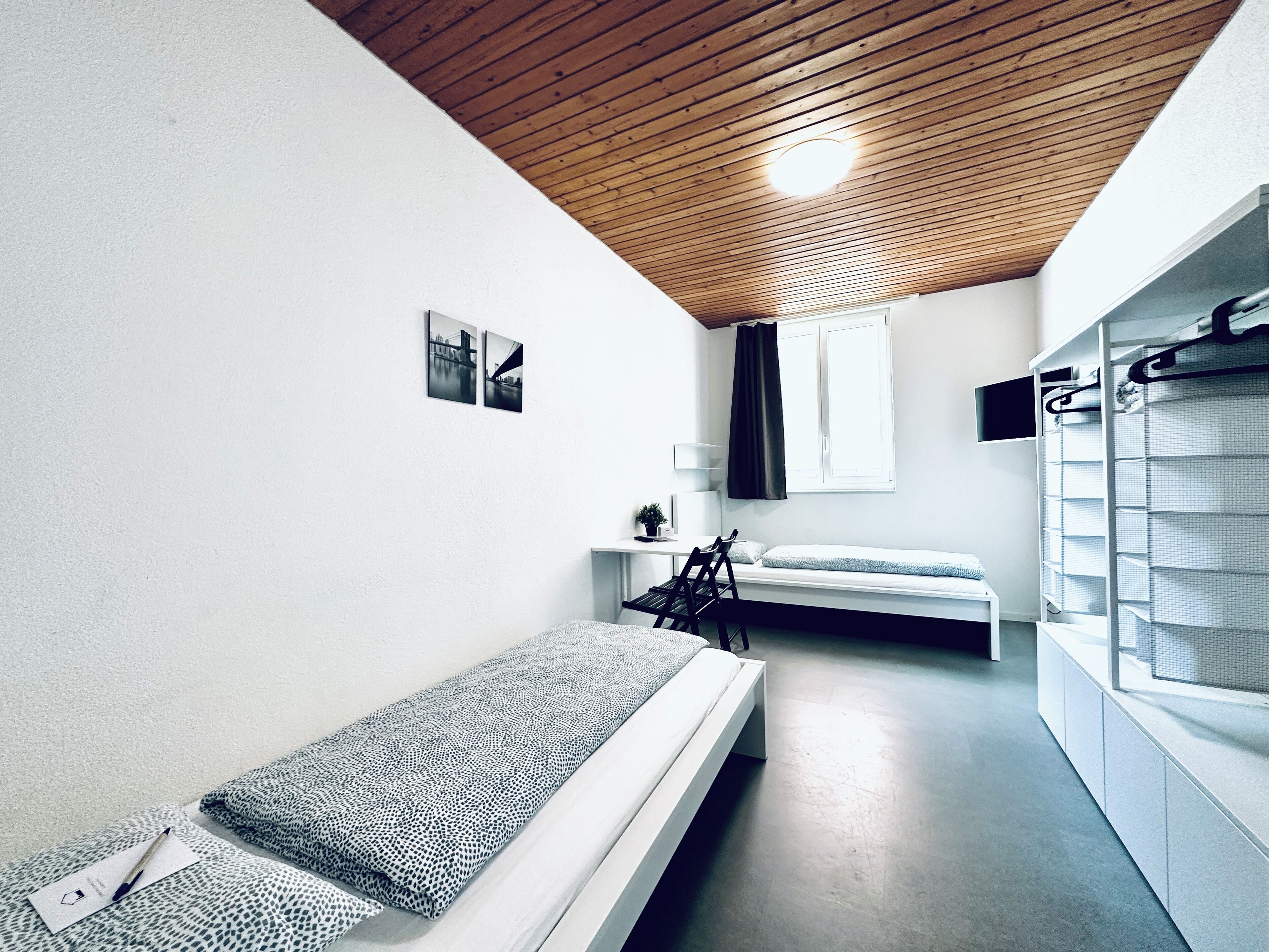 Une petite pièce comprenant un lit superposé, un bureau, une chaise, un porte-vêtements et une fenêtre avec un rideau.