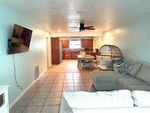 A living room with a sofa, a TV mounted on the wall, and a dining area with a table and chairs. - 1 block to the beach, awesome! (Cocoa Beach)