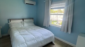 Et soveværelse med en seng, et vindue med gardiner, en loftlampe og en vægmonteret aircondition.