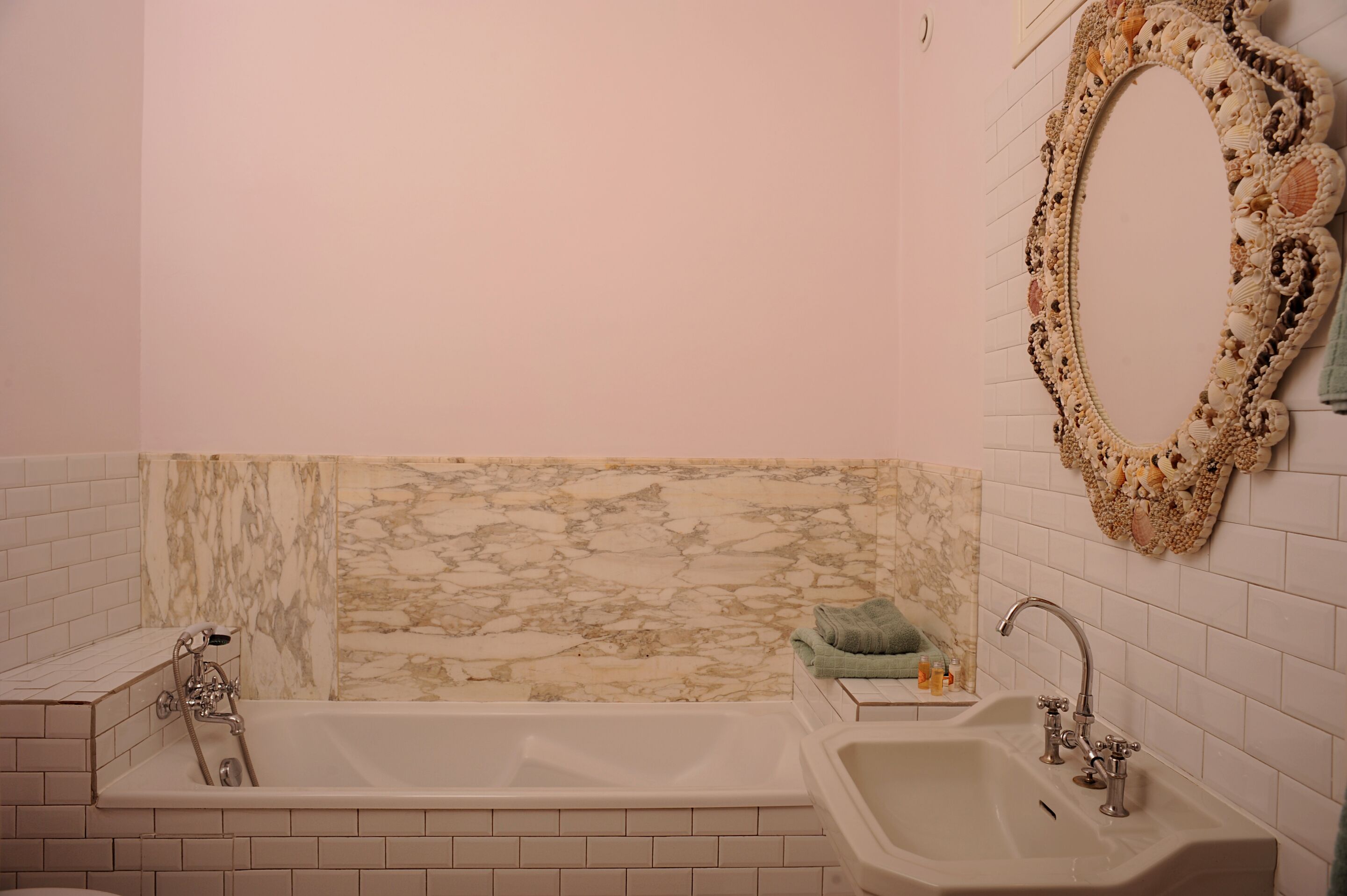 Un baño con pared de mármol, una bañera grande, un lavabo y un espejo decorativo con marco de concha marina.
