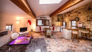 Una sala de estar acogedora con televisión, una mesita de centro y una chimenea. Hay una zona de cocina con una pared de piedra y techo de madera.