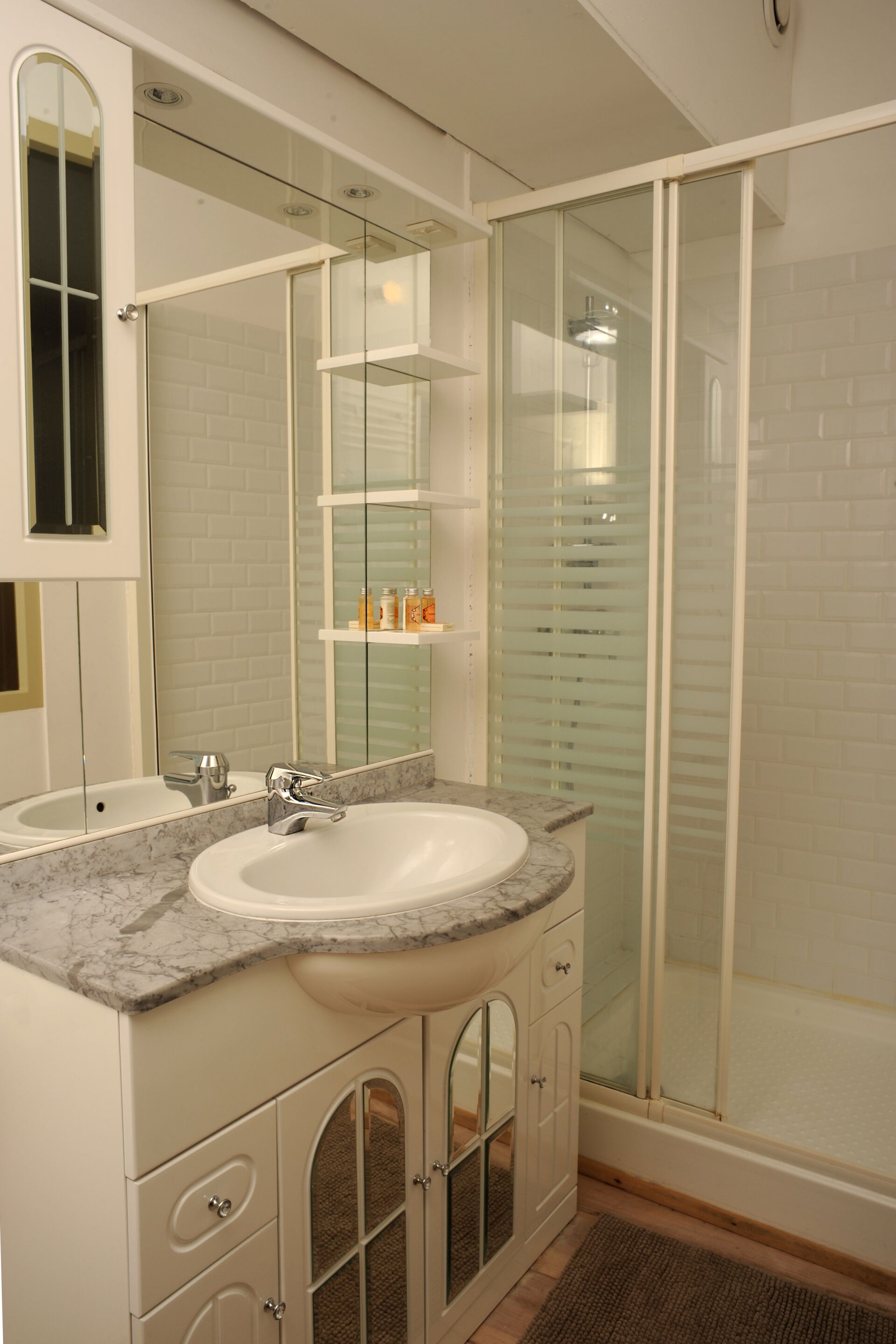 A bathroom with two sinks, a glass shower enclosure, and a mirror with a shelf above it.
