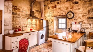 Una cocina rústica con paredes de piedra, una lavadora, un lavamanos y una mesa de comedor de madera.