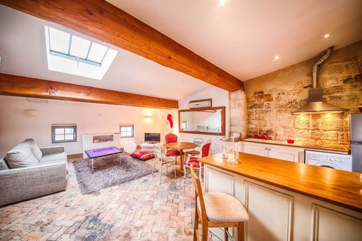A cozy living room with a fireplace, a dining area, and a kitchen with stone walls and wooden beams.