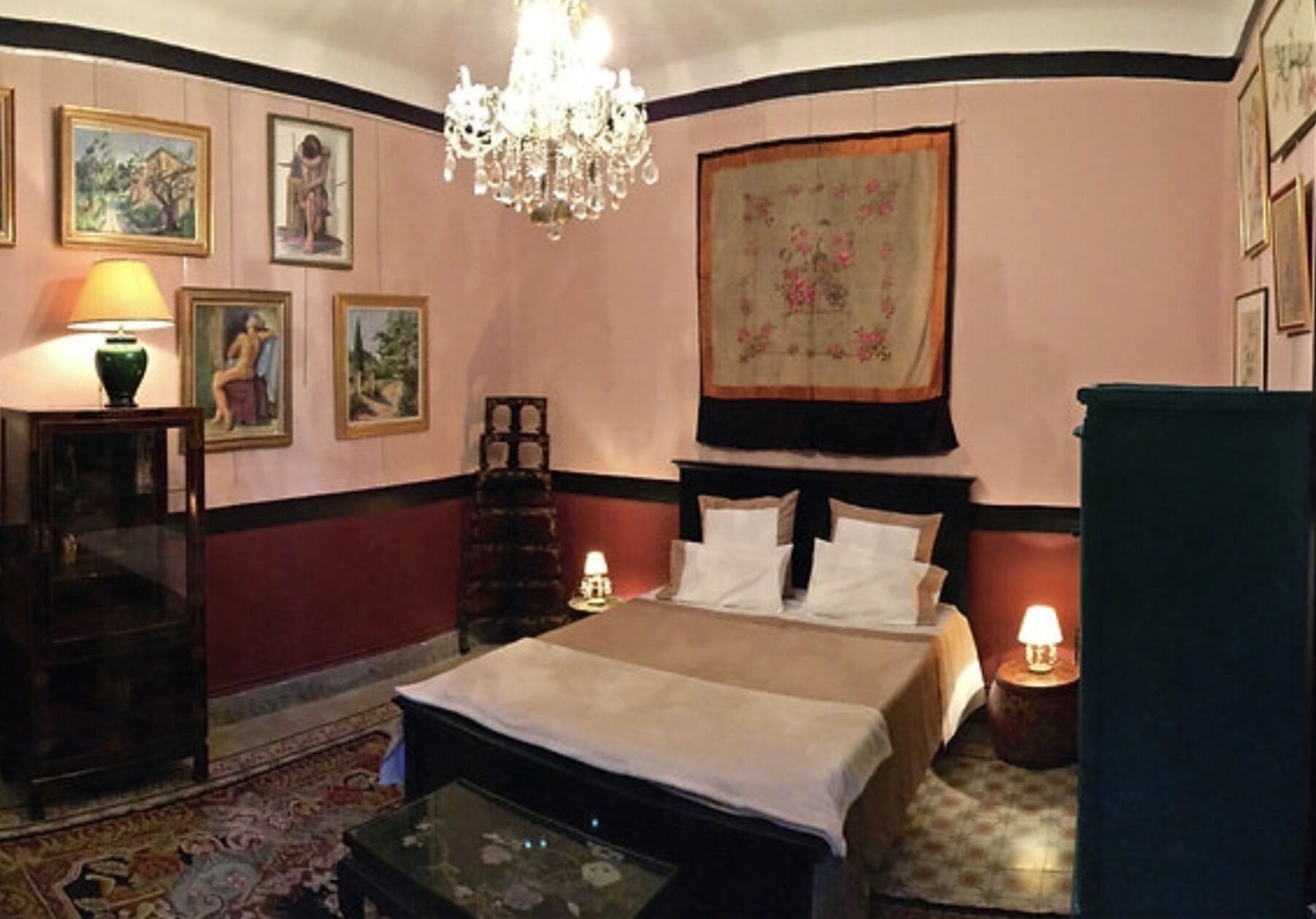 A hotel room with a bed, a chandelier, a table, and a rug.