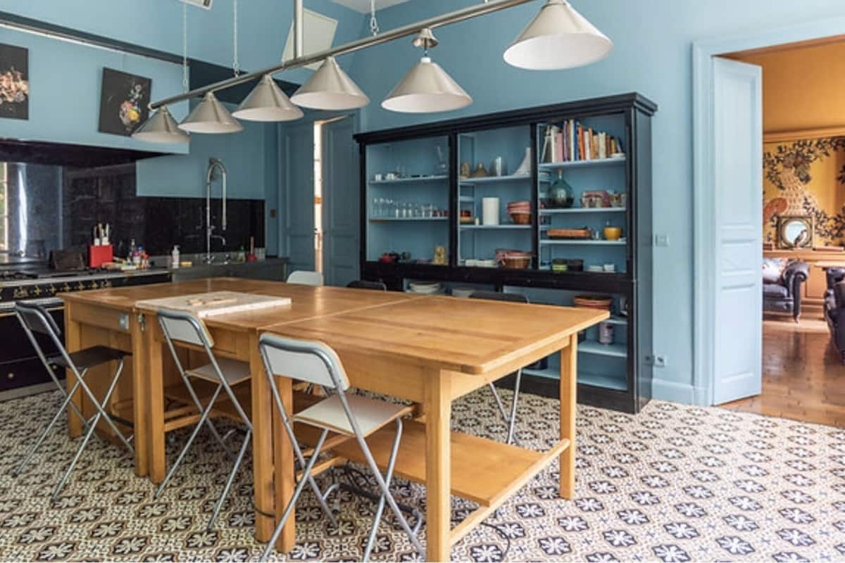 A kitchen with a wooden table and chairs, a black bookshelf, and pendant lights.