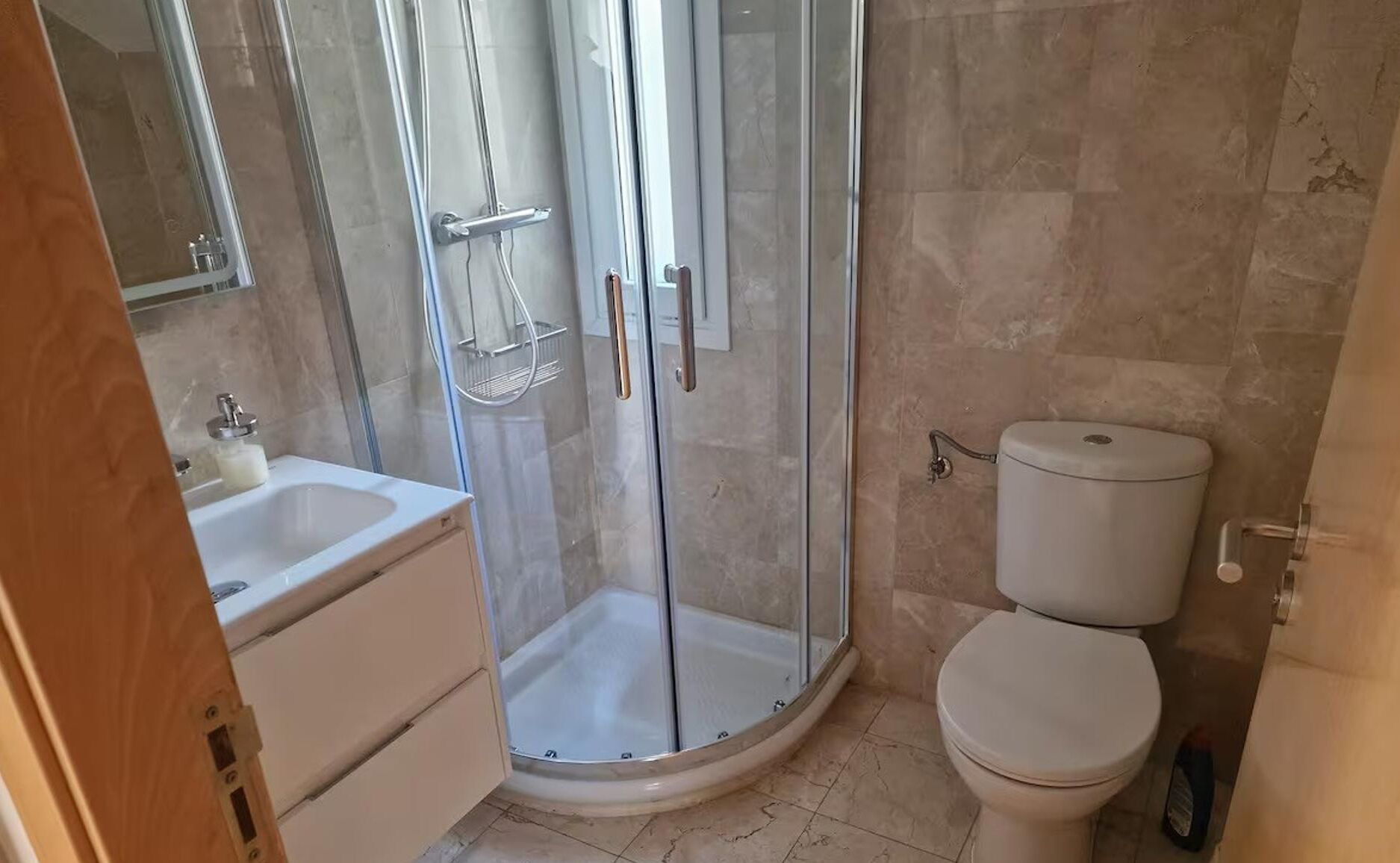 A bathroom with a glass-enclosed shower, a toilet, and a sink.