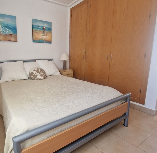 Une chambre à coucher comprenant un lit, une table de chevet, une armoire en bois et deux tableaux accrochés au mur.