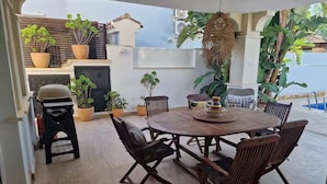 Eine Terrasse mit einem runden Holztisch und Stühlen, umgeben von Topfpflanzen und einer hängenden Dekoration.