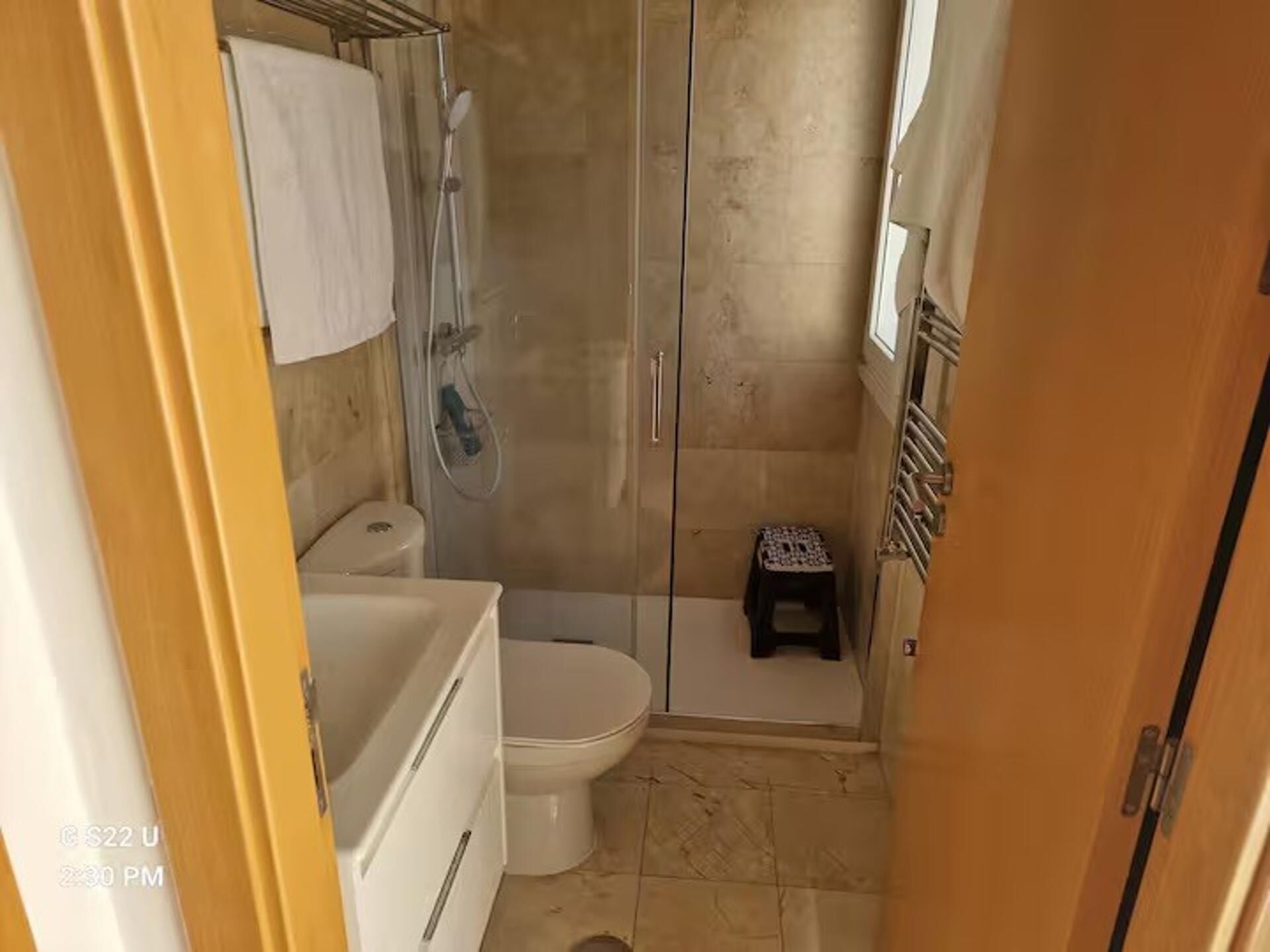 A compact bathroom with a shower, toilet, and a small stool.