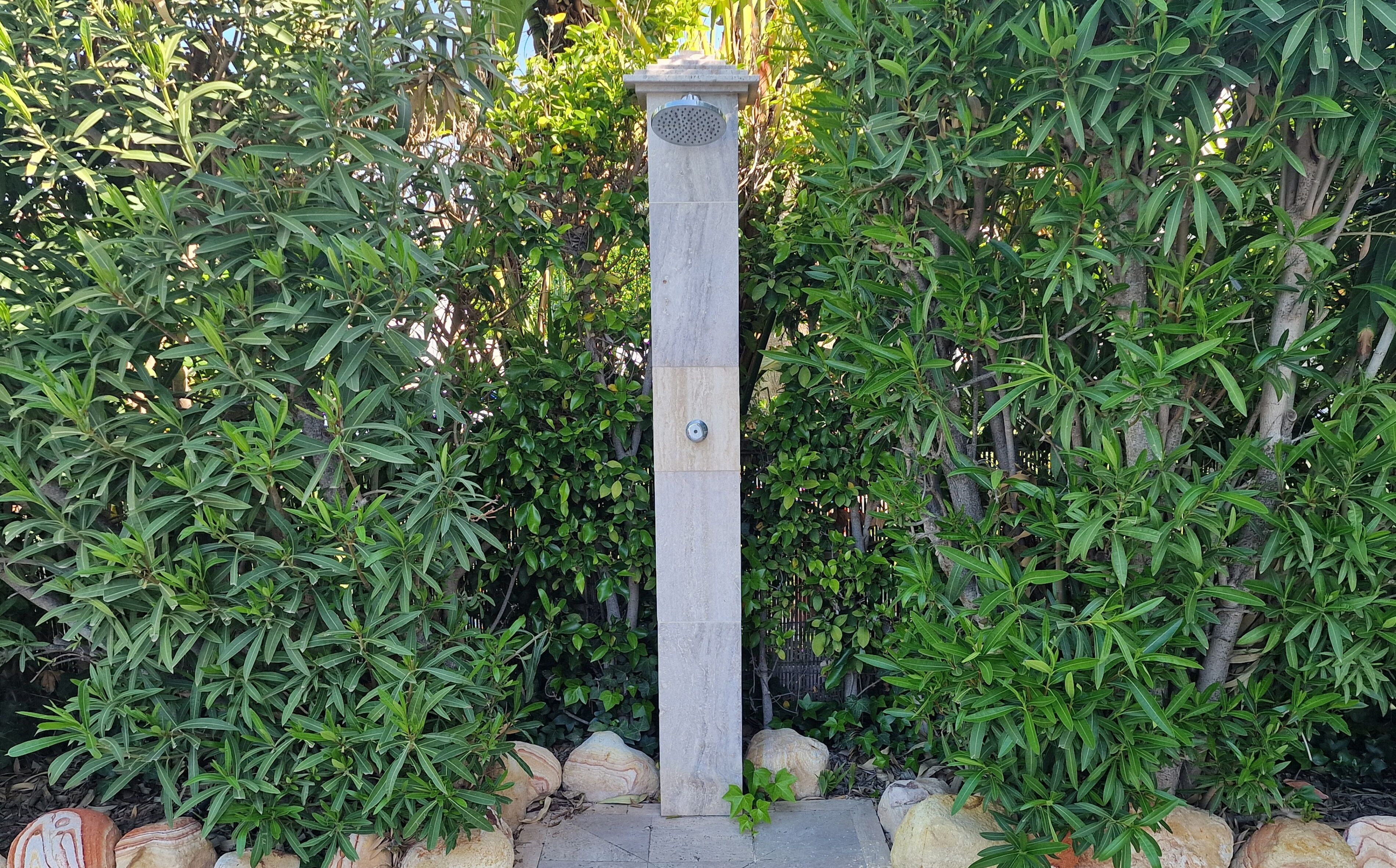 A tall, narrow stone pillar with a circular metal plaque, surrounded by dense green foliage.