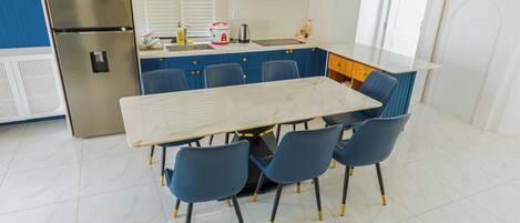 Una cocina moderna con encimera de mármol, refrigerador de acero inoxidable, sillas azules y armarios blancos.