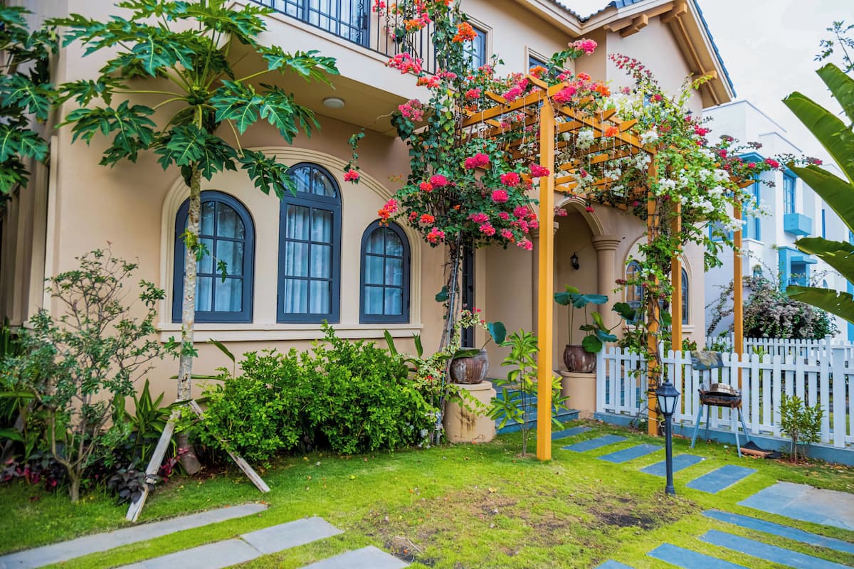 Una casa con jardín, una pérgola florida y una cerca de piquetes blancos.