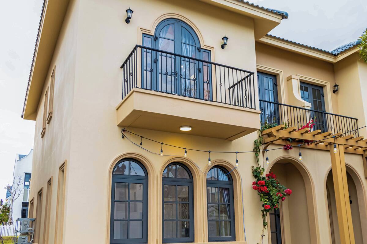 Una casa de dos pisos con balcón, ventanas en arco y un pequeño porche.