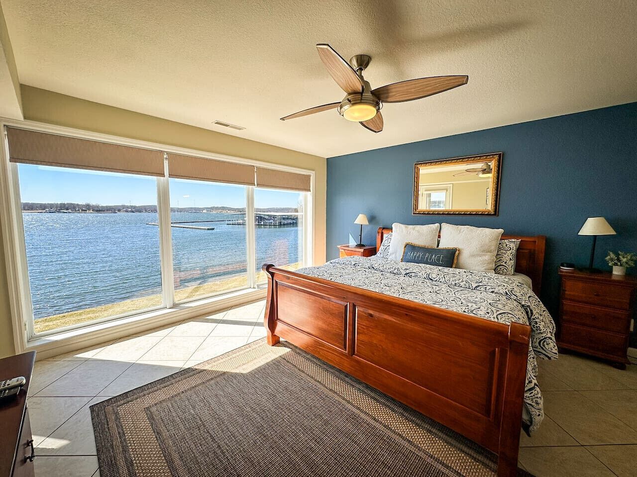 A bedroom with a large bed, a ceiling fan, a nightstand, and a view of the water.