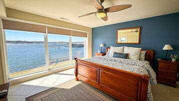 A bedroom with a large bed, a ceiling fan, a nightstand, and a view of the water.